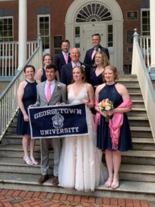 a family in wedding attire poses on exterior stairs with a Georgetown University banner