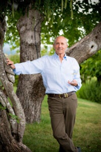a man holding a wineglass stands next to a tree