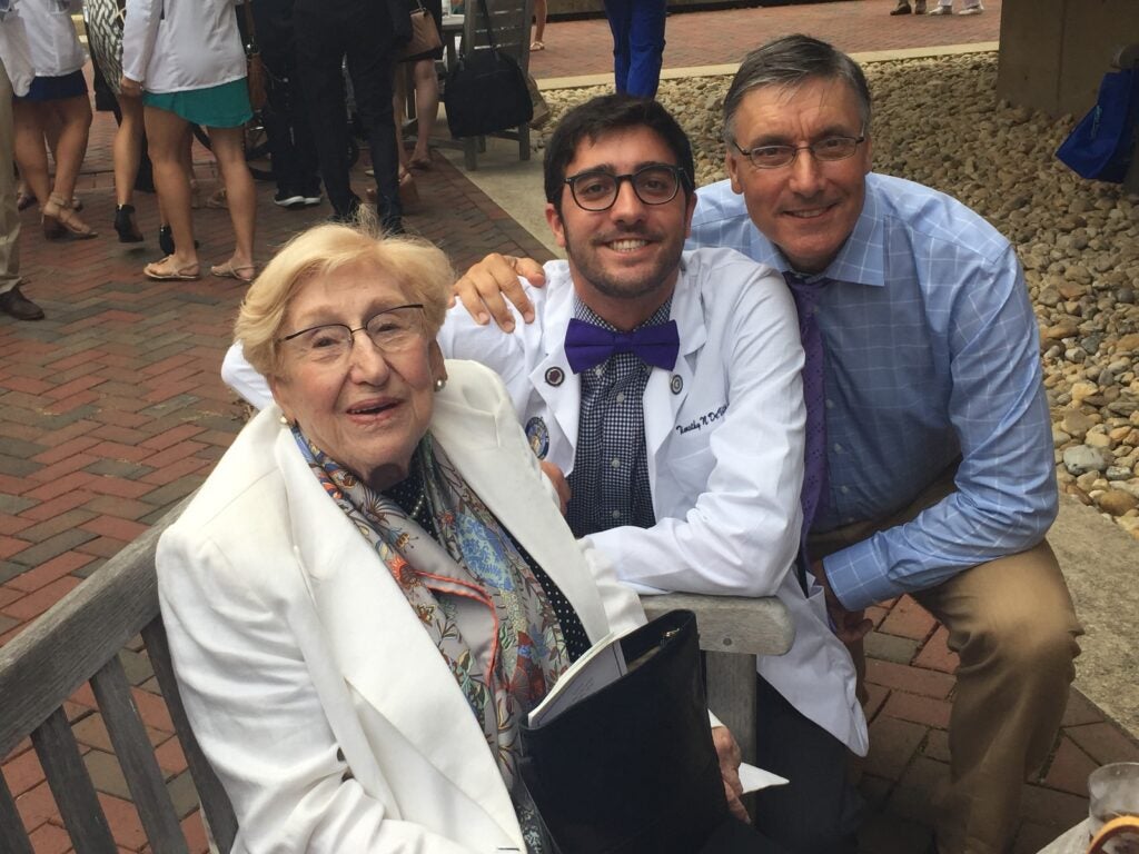 a woman in a white medical coat sits on a bench and smiles with two people
