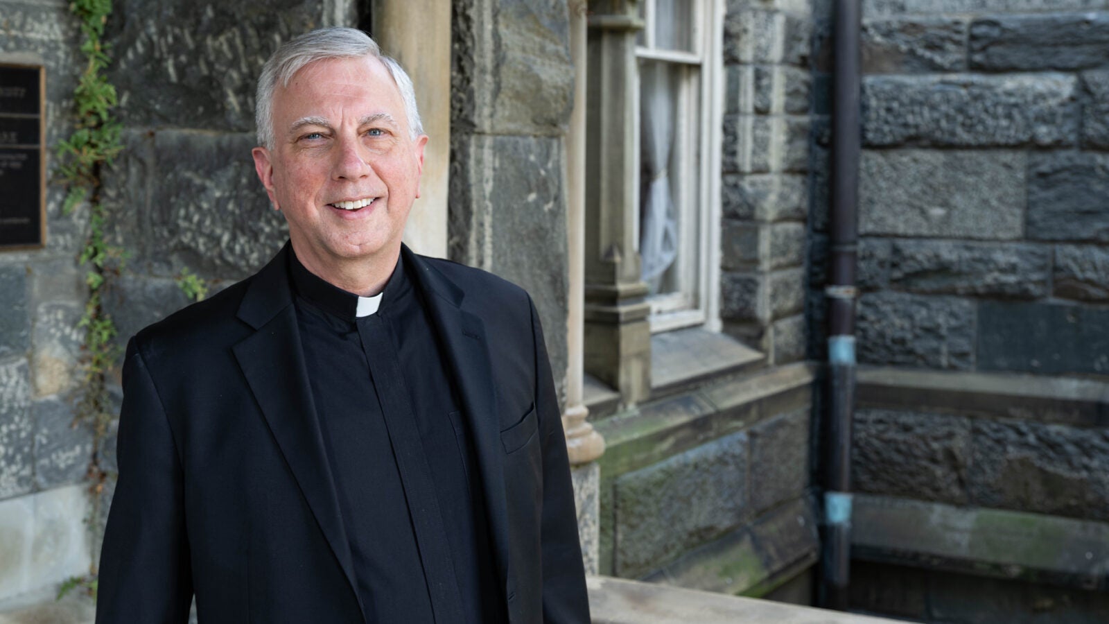 a man in clerical wear stands in front of a stone building