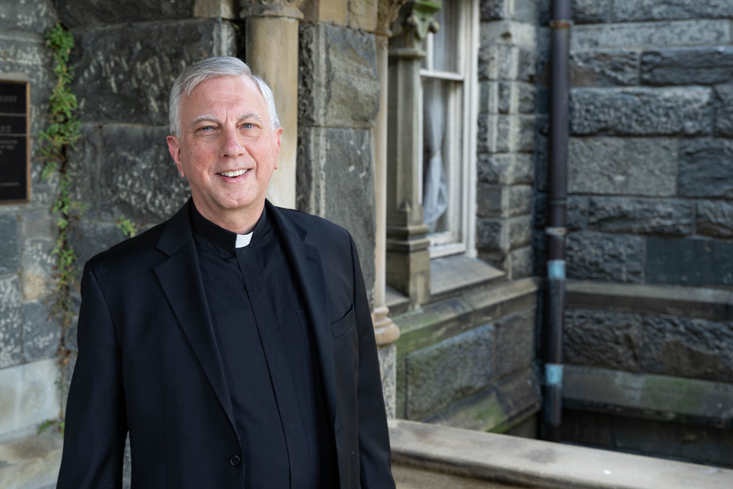 a man in clerical wear stands in front of a stone building