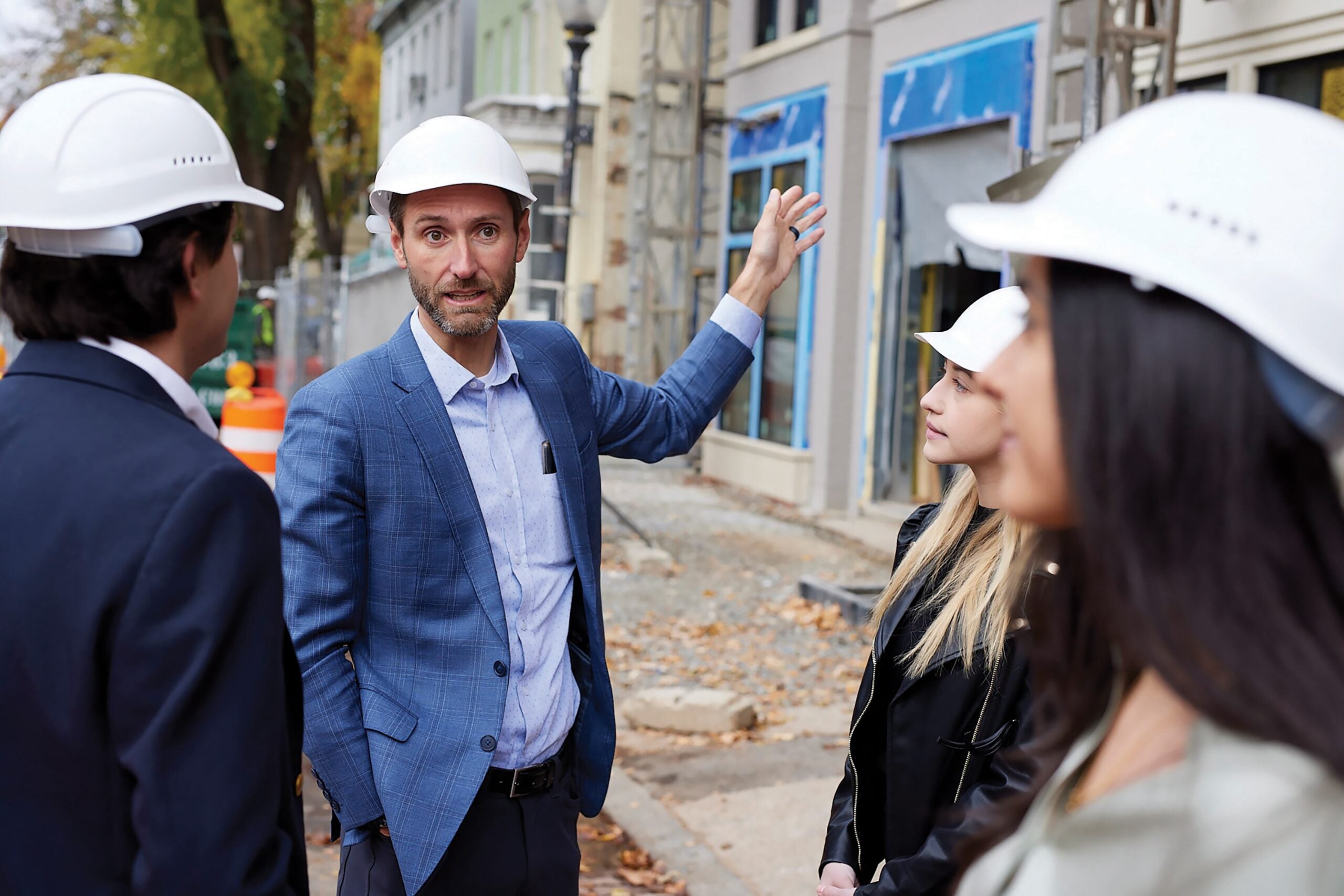 person in suit and hard hat gestures towards building
