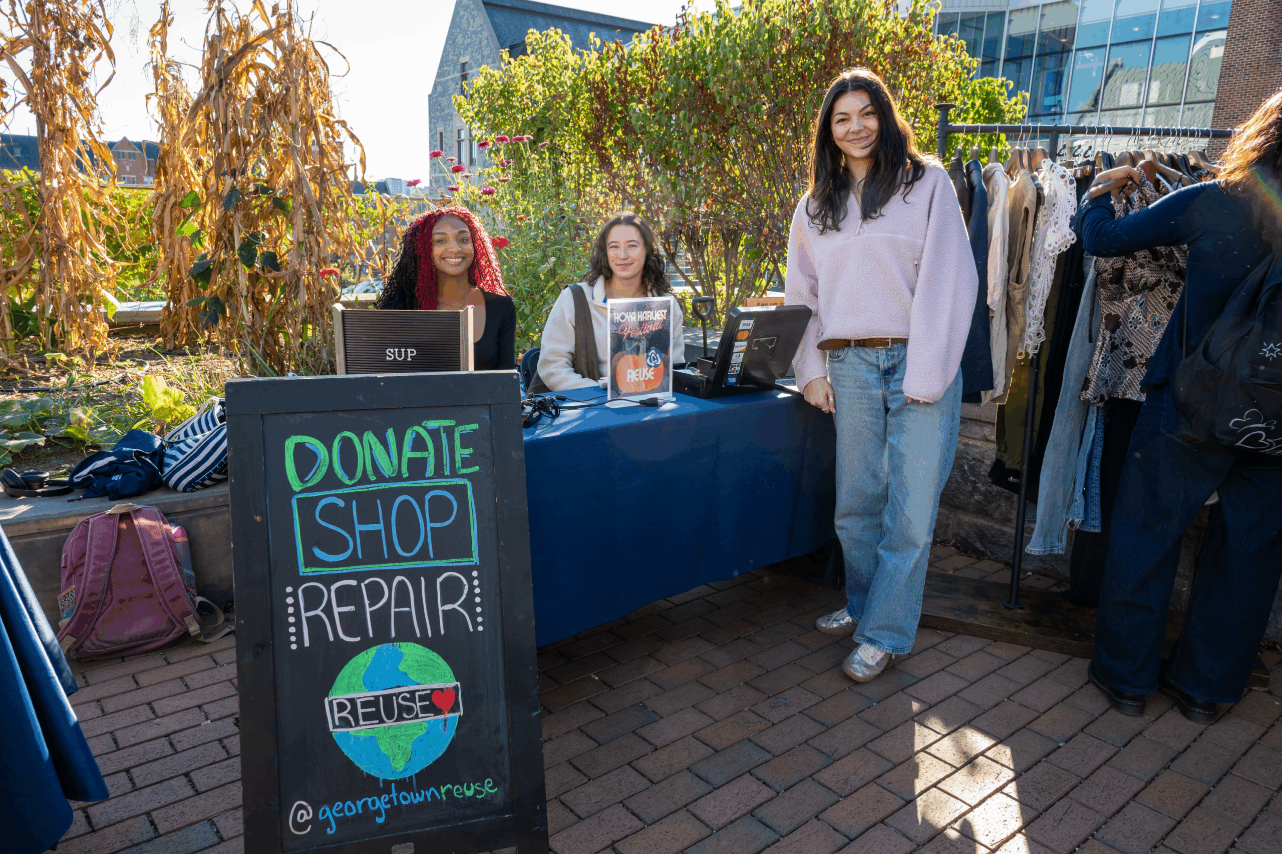 three people at at a table outside with a sign that says "donate, shop, repair"