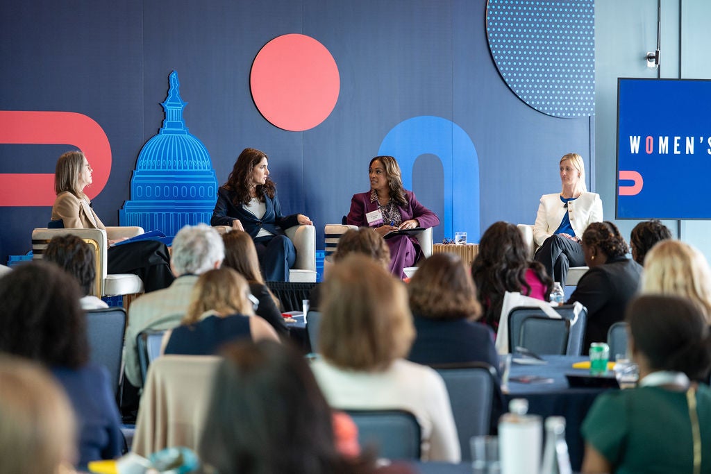 four women sitting in chairs on a stage in front of a crowded conference room 