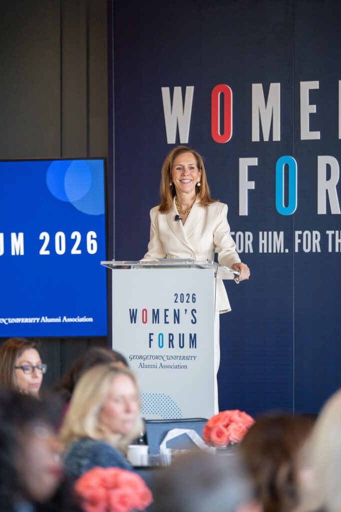 a woman onstage at a podium which has the words "2026 Women's Forum" across it 