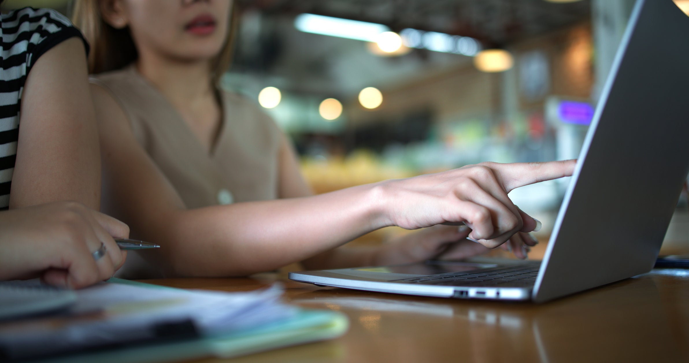 Young woman's hand pointing at laptop at coffee shop.