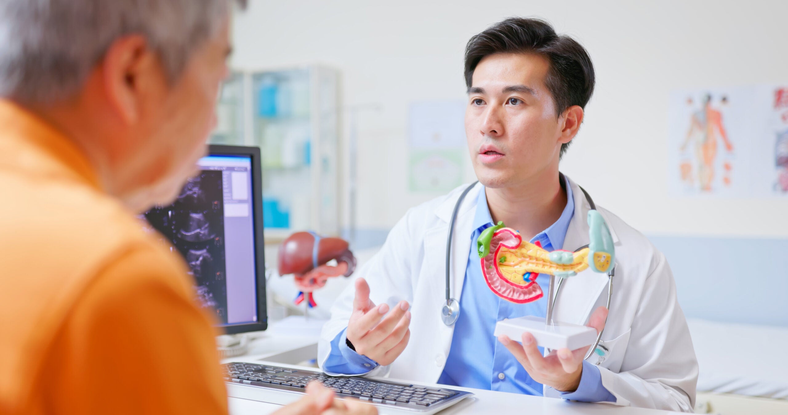 closeup back view asian doctor explains pancreas and spleen issues to elderly patient using 3d anatomy model with ultrasound equipment in gastroenterology department with possible cancer diagnosis